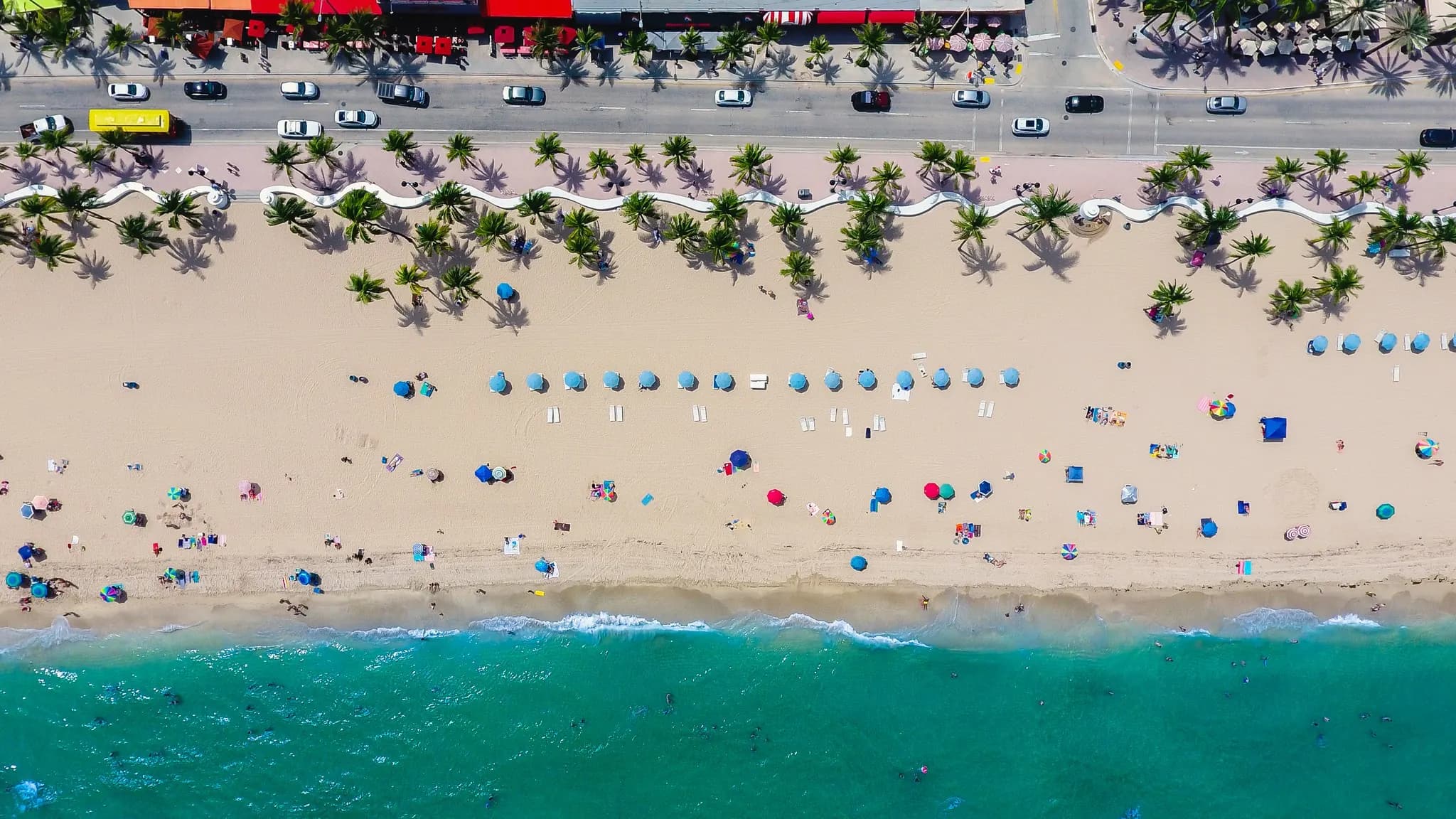 Aerial view of Fort Lauderdale Beach with umbrellas, palms and the white wave wall along A1A
