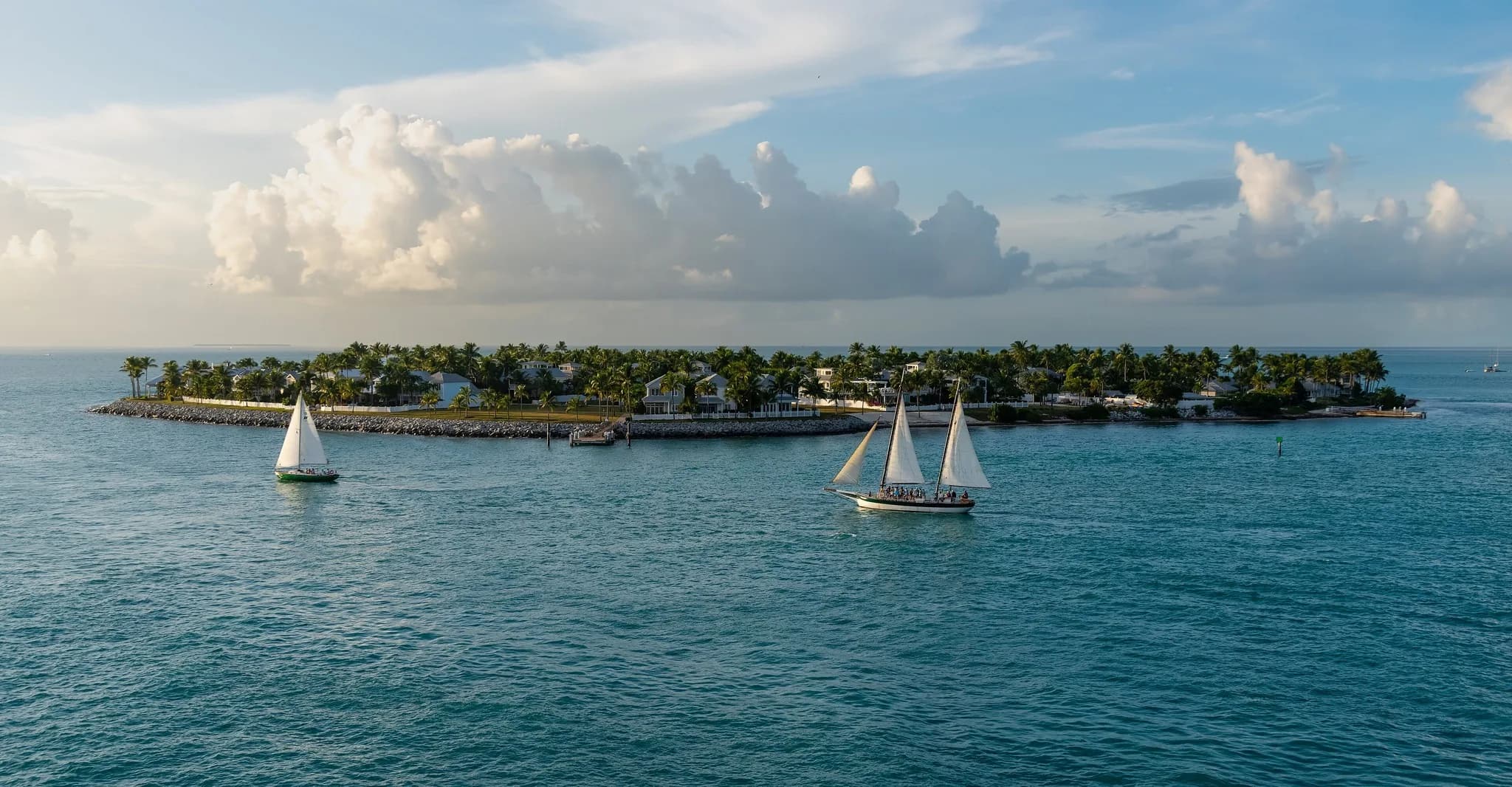 Two sailboats on blue water off Key West with Sunset Key and its palms behind