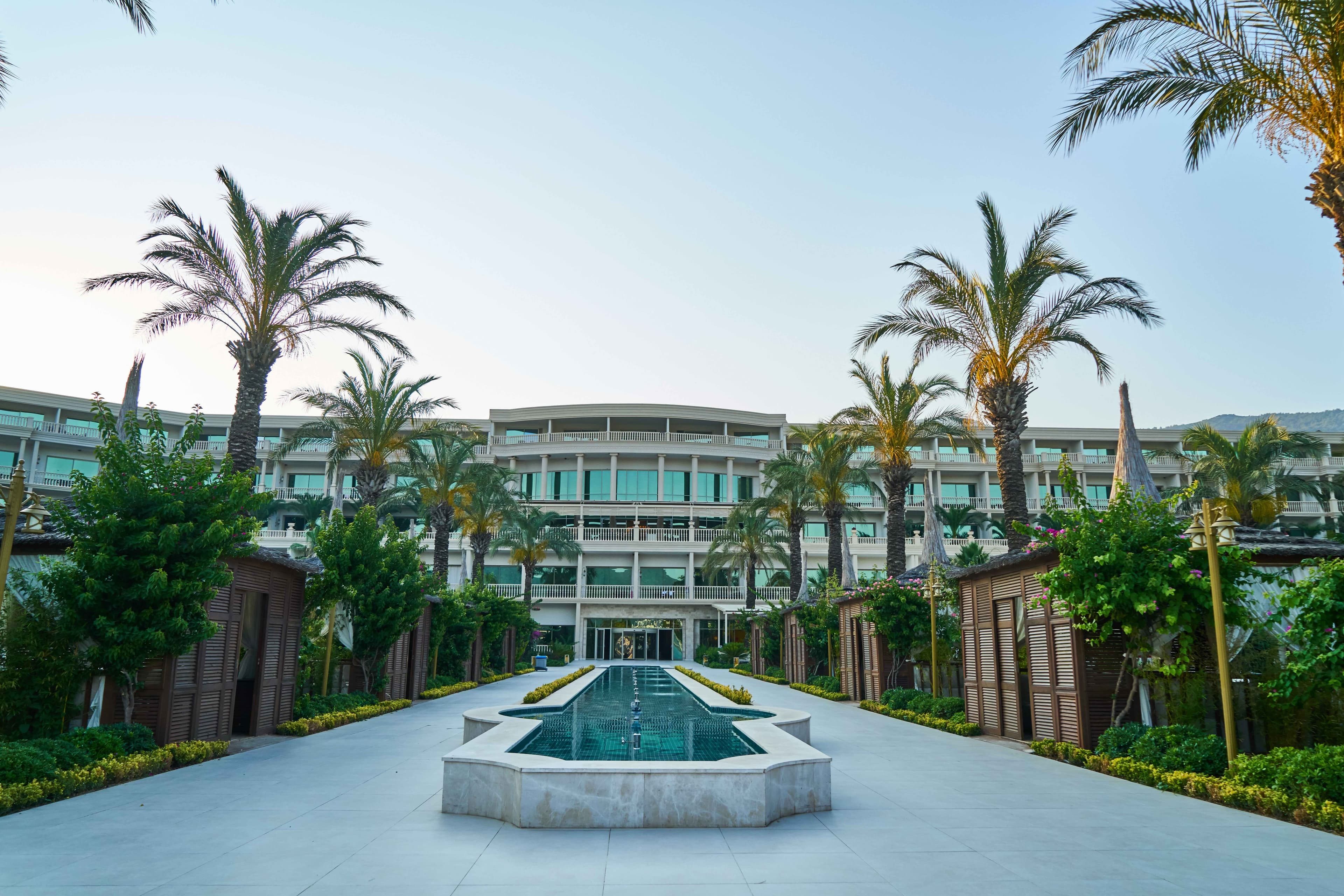 Long reflecting pool lined with palm trees leading to a white multistory luxury gay resort building