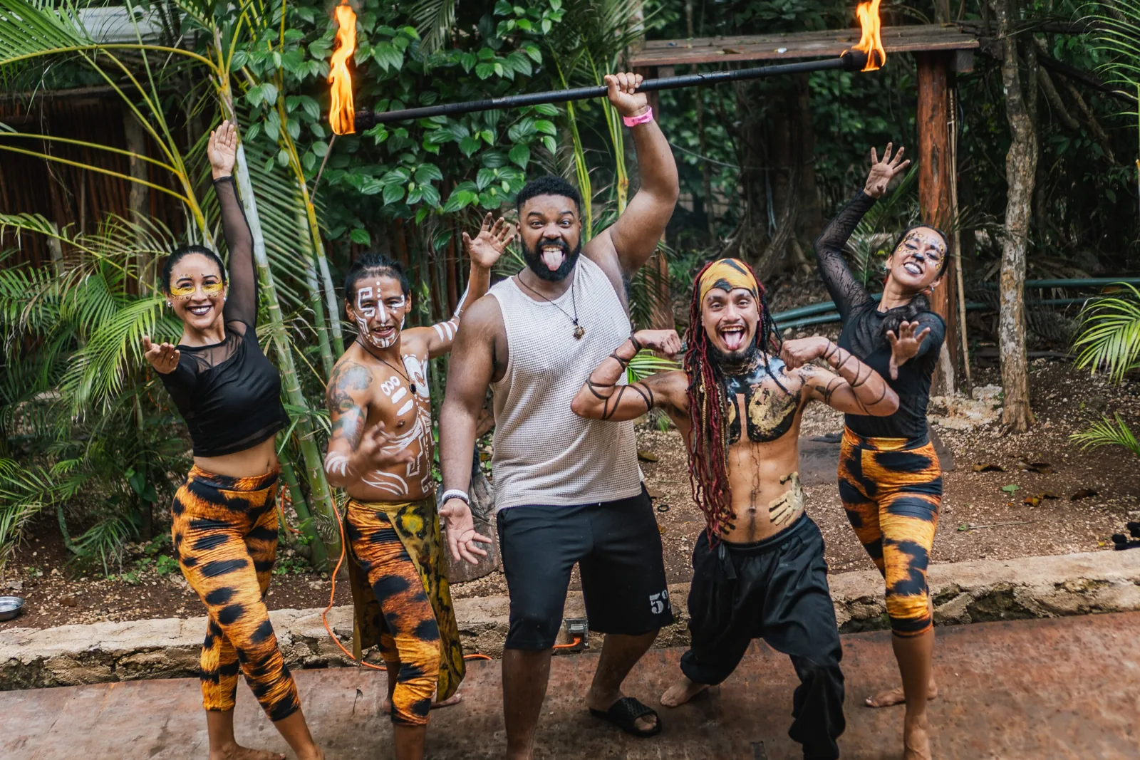 A man joyfully posing with indigenous performers in tribal body paint, surrounded by lush greenery.
