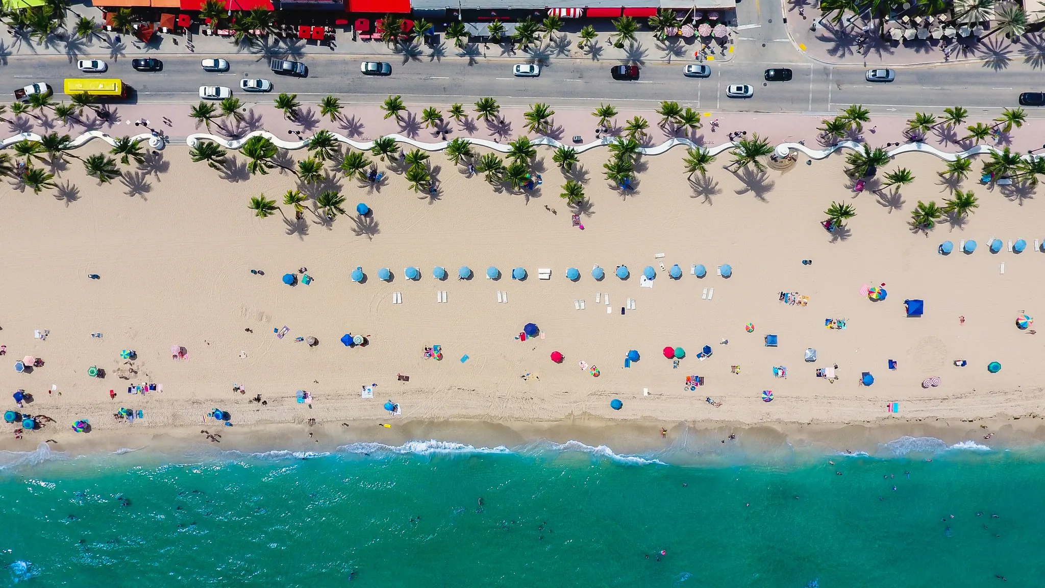 Aerial view of Fort Lauderdale Beach with umbrellas, palms and the white wave wall along A1A