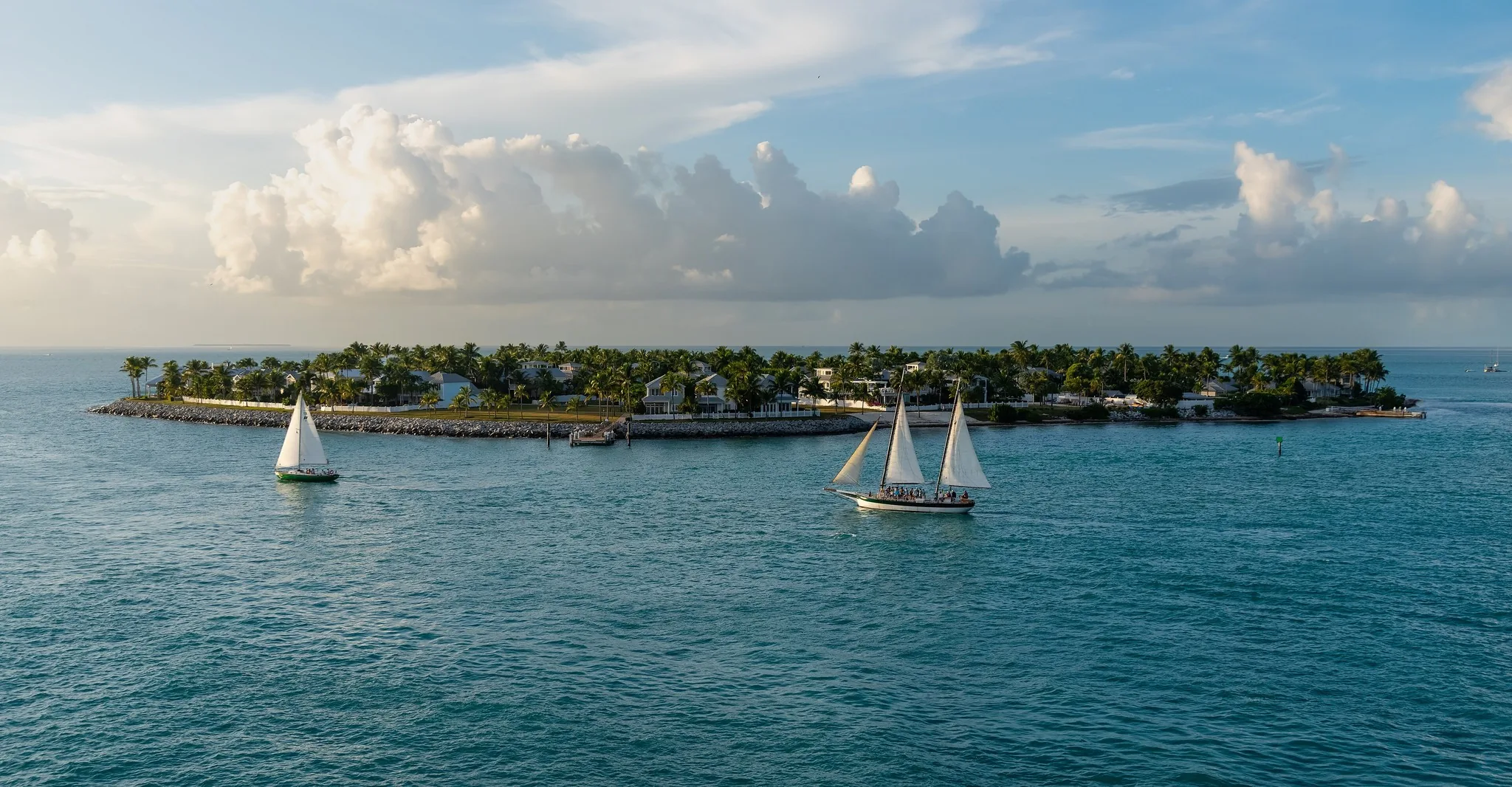 Two sailboats on blue water off Key West with Sunset Key and its palms behind