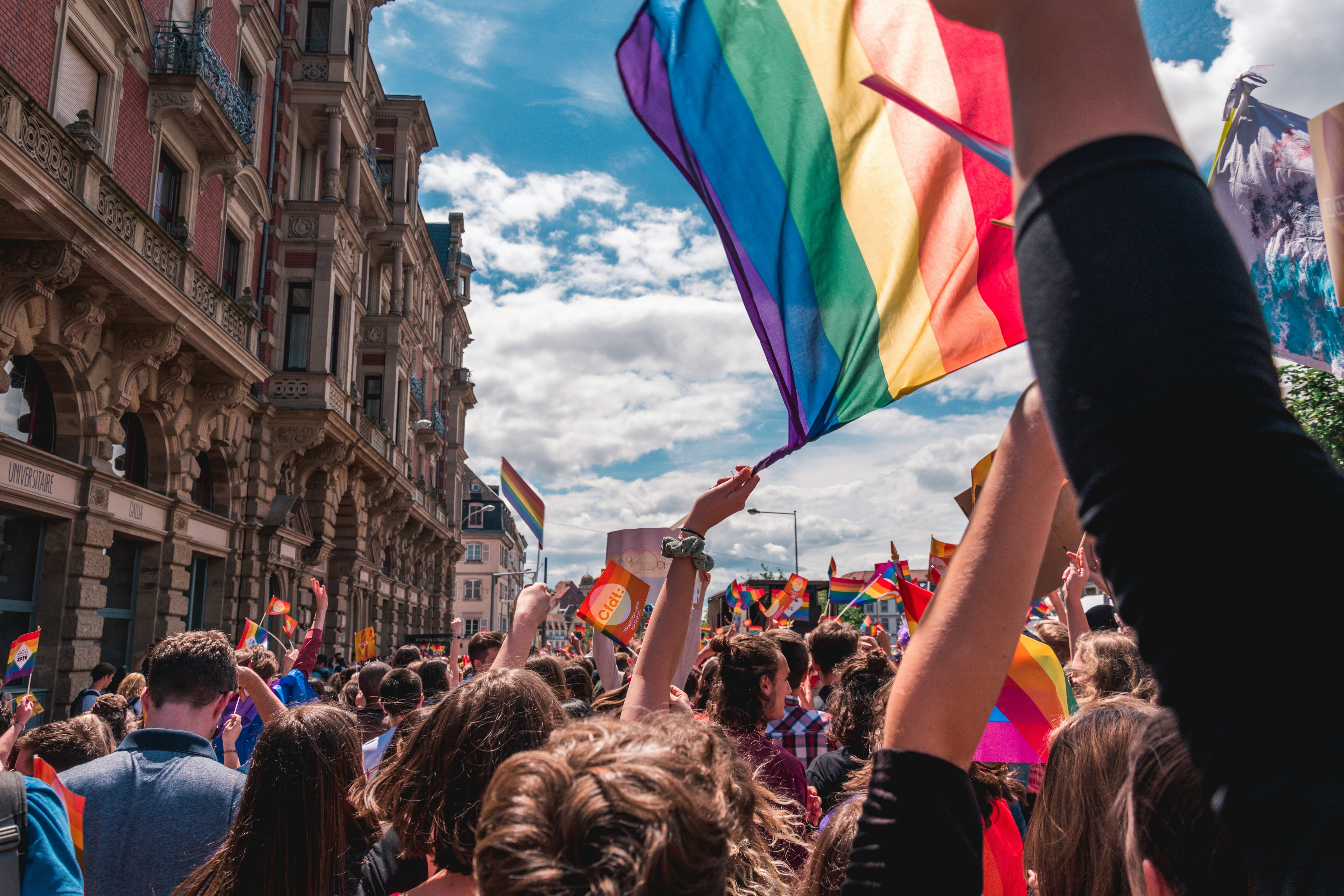 A crowd of people and an LGBTQ+ flag being waved