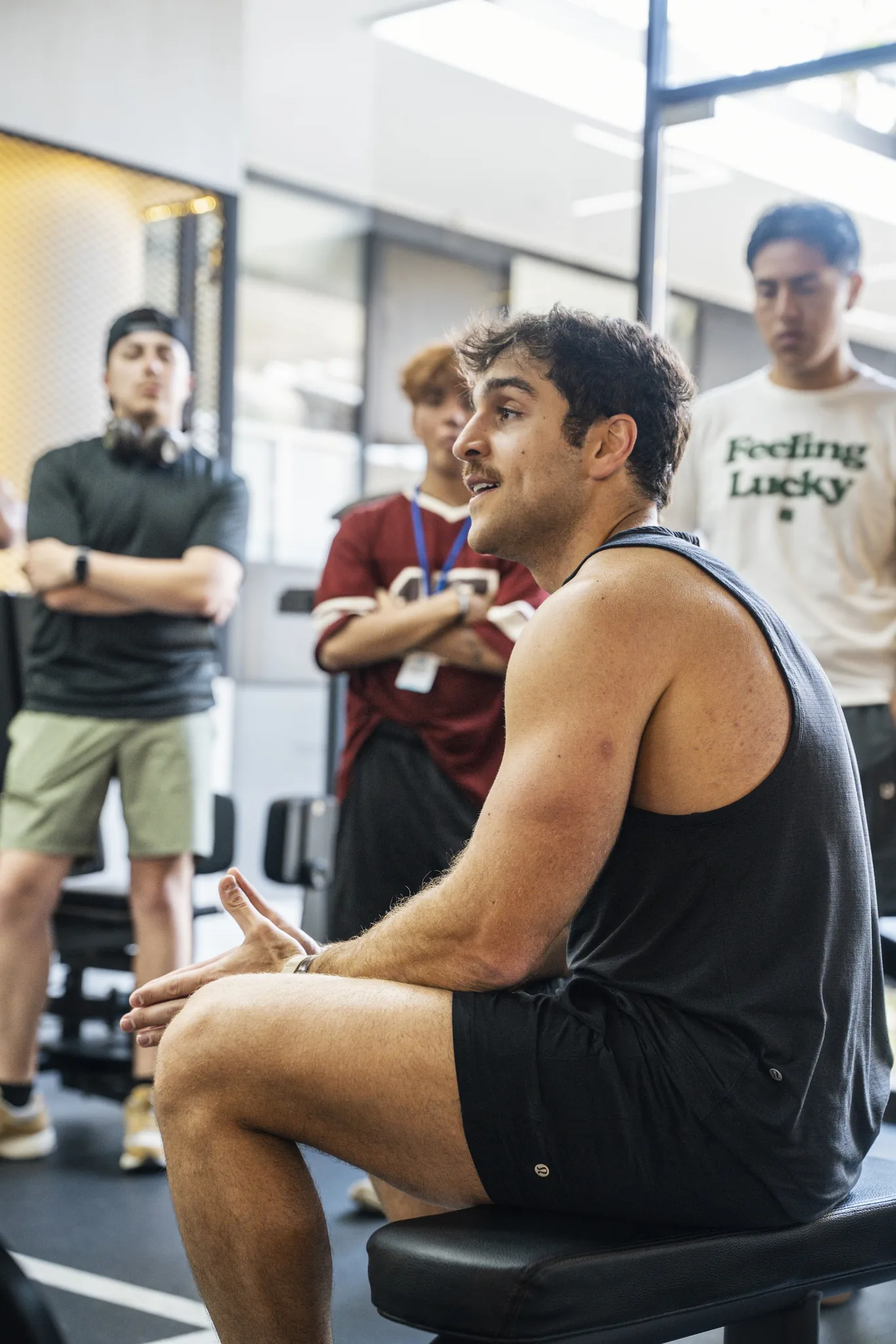 A coach sitting on a bench leading a group talk with retreaters standing around him at the gym
