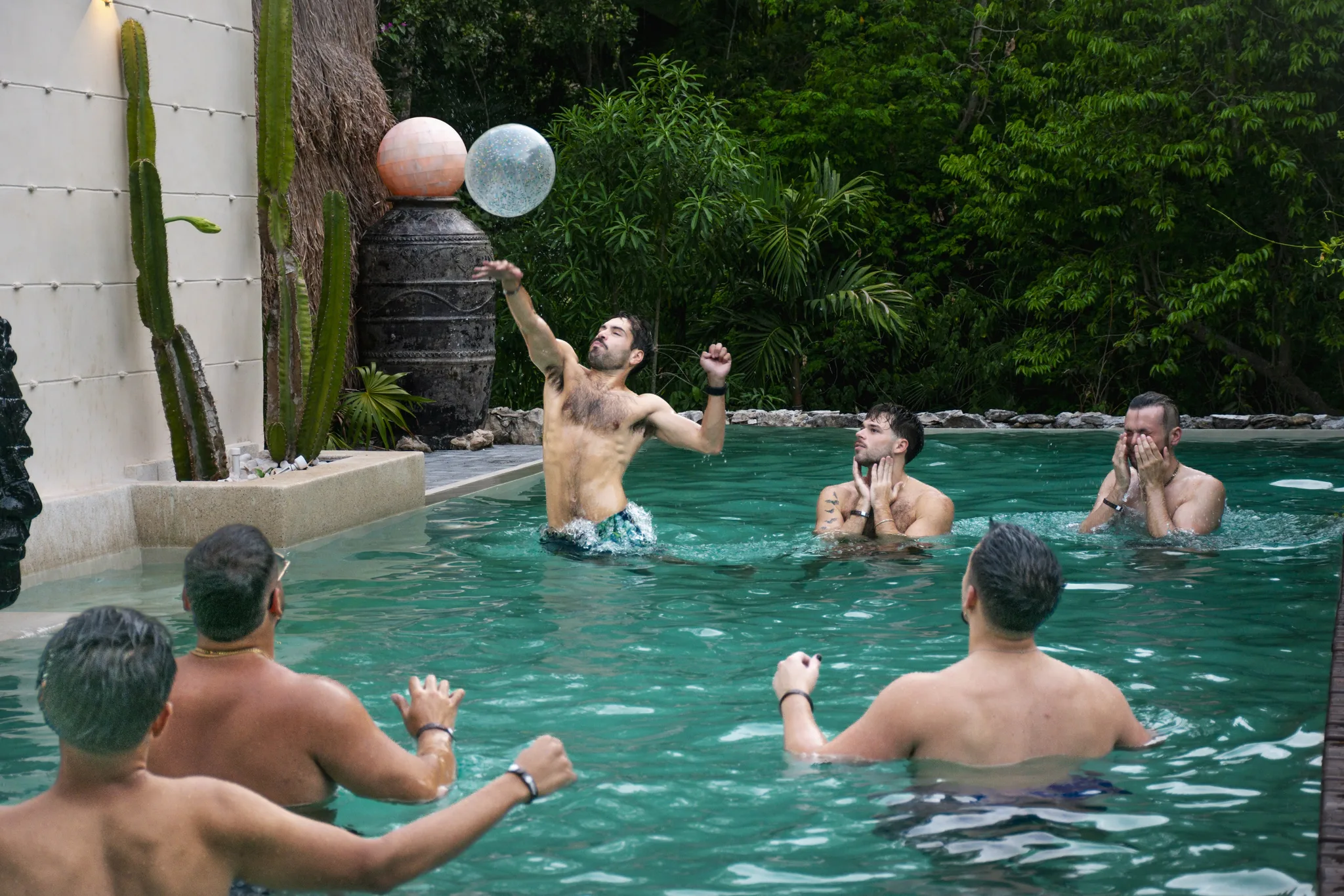 Retreaters playing with a beach ball in a villa pool surrounded by cactus and jungle