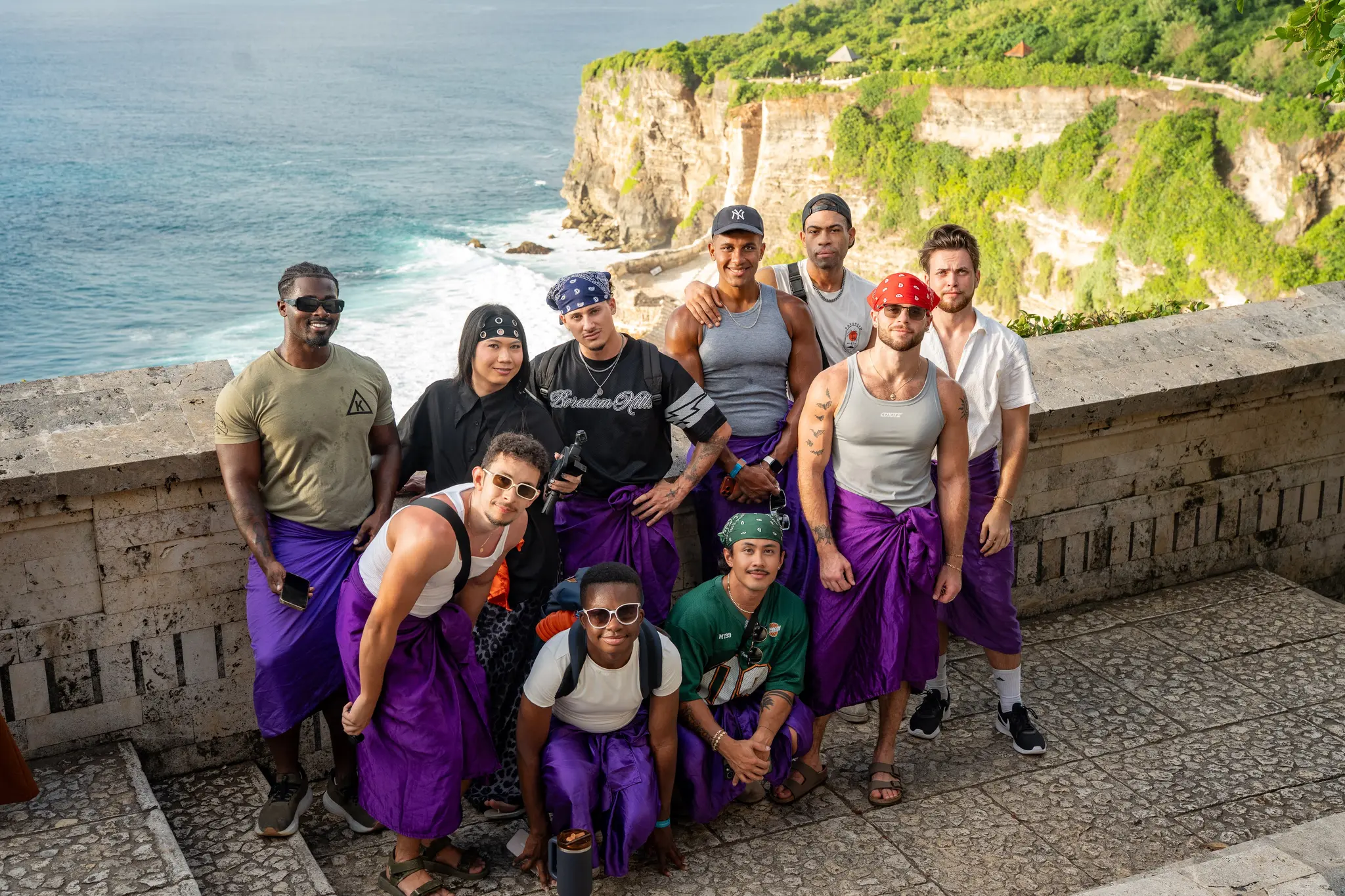 Visiting Wrld retreaters in purple sarongs on the cliff terrace at Uluwatu temple above the ocean in Bali
