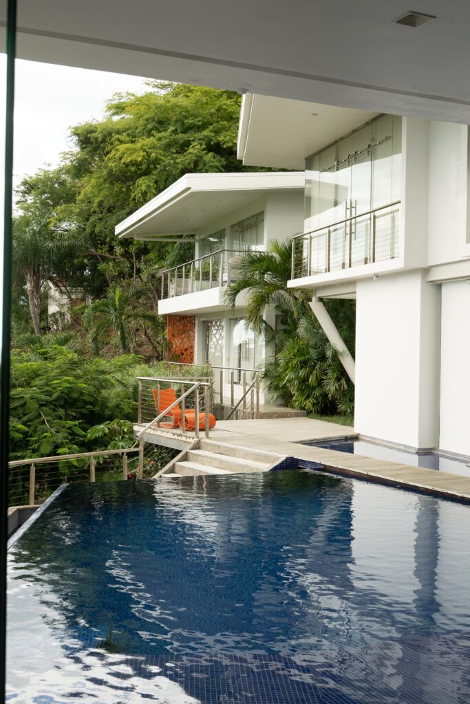 A mountain-side home with three room balcony and an infinity pool with trees.