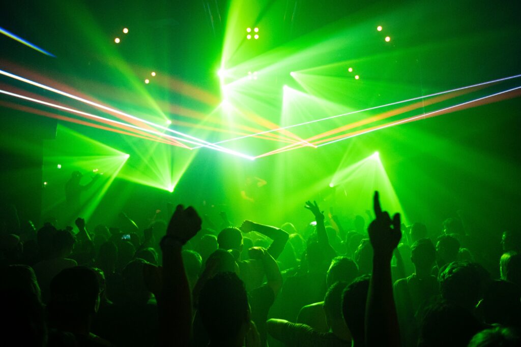 A crowd of people facing neon green, blue and red strobe lights